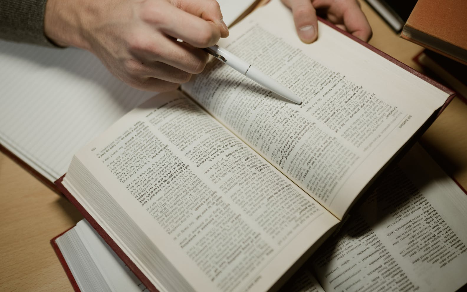 A hand holding a pen while studying an open book, highlighting learning and education.