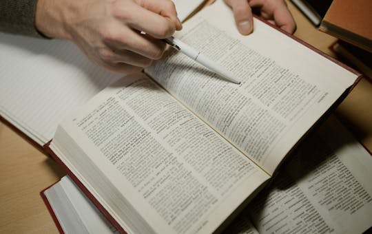 A hand holding a pen while studying an open book, highlighting learning and education.