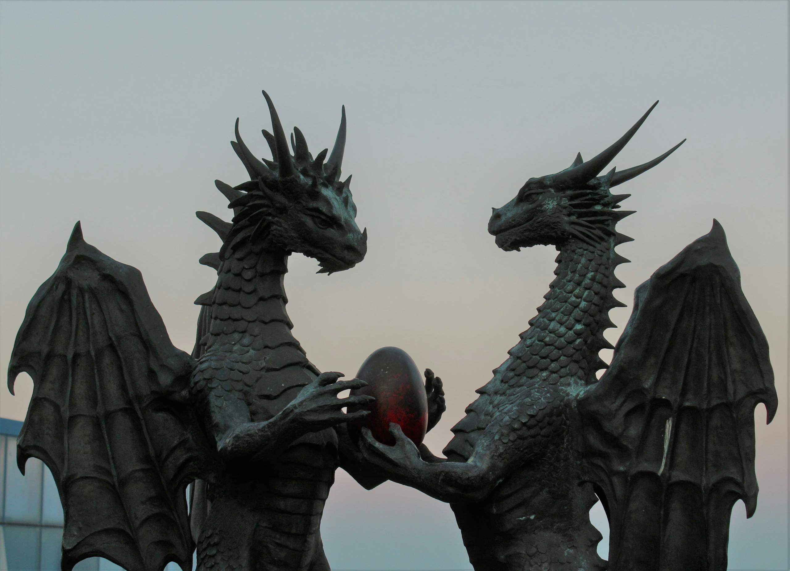 Two impressive dragon sculptures holding an enigmatic egg against a twilight sky, symbolizing fantasy and myth.