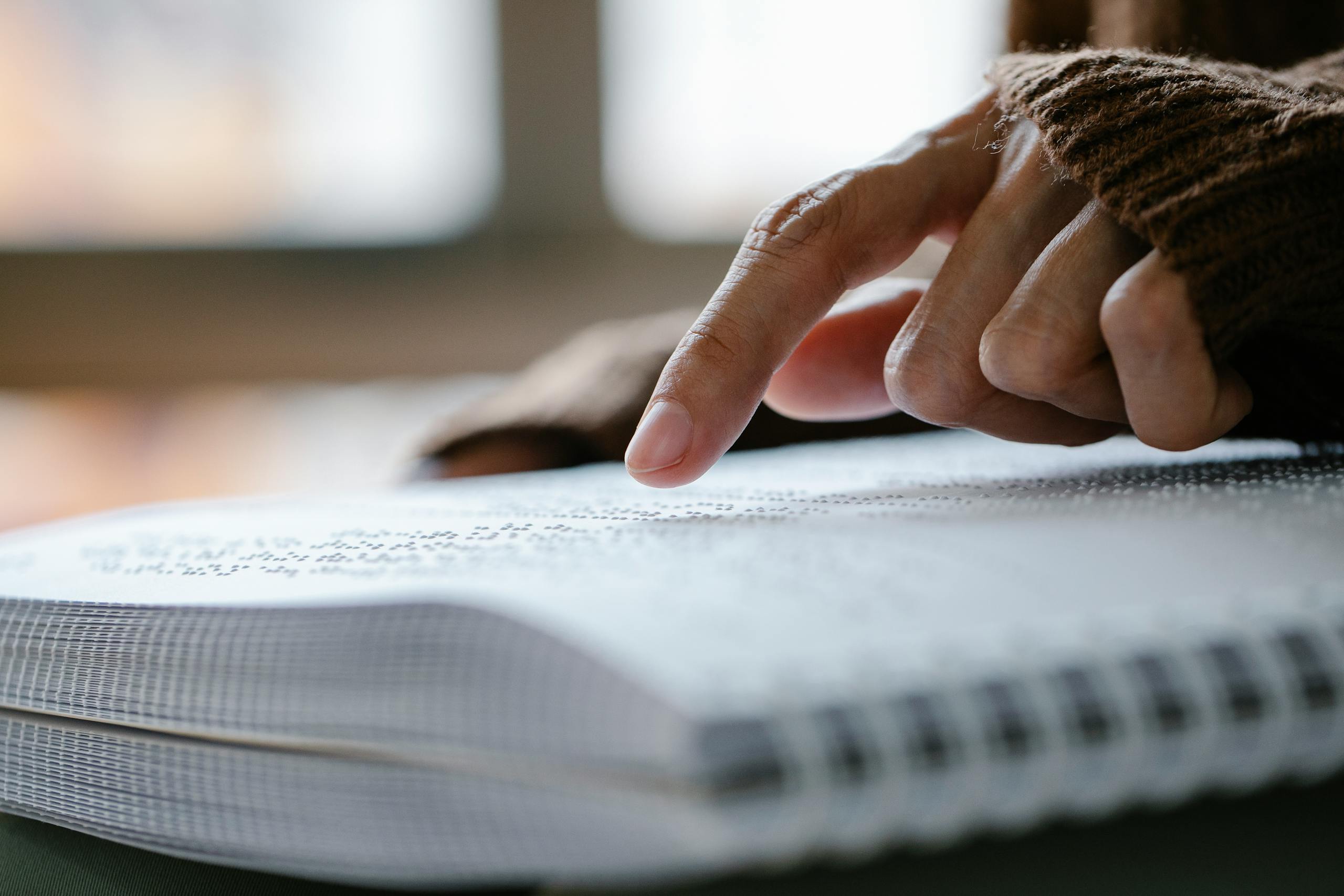 A hand carefully traces over embossed Braille text, emphasizing tactile reading.
