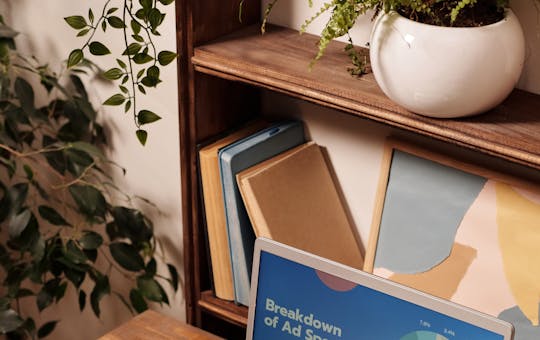 Laptop displaying ad spend data on a wooden desk with office supplies.